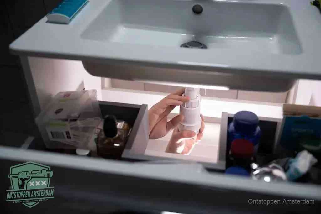 Een pompfles met zeep boven een wastafel, de heet water en afwasmiddel-methode om een vetprop in de afvoer los te maken in Amsterdam