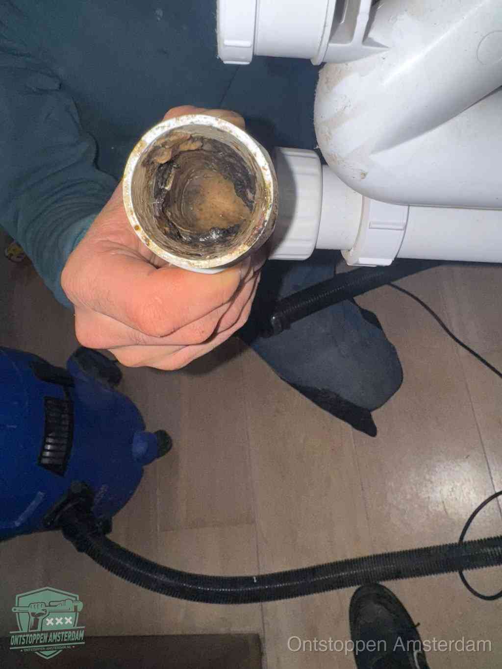 Een hand houdt een losgekoppeld PVC-afvoerbuisstuk vast dat van binnen volledig is dichtgeslibd met vet, vuil en aanslag, de meest voorkomende oorzaak van een verstopte afvoer in Amsterdam