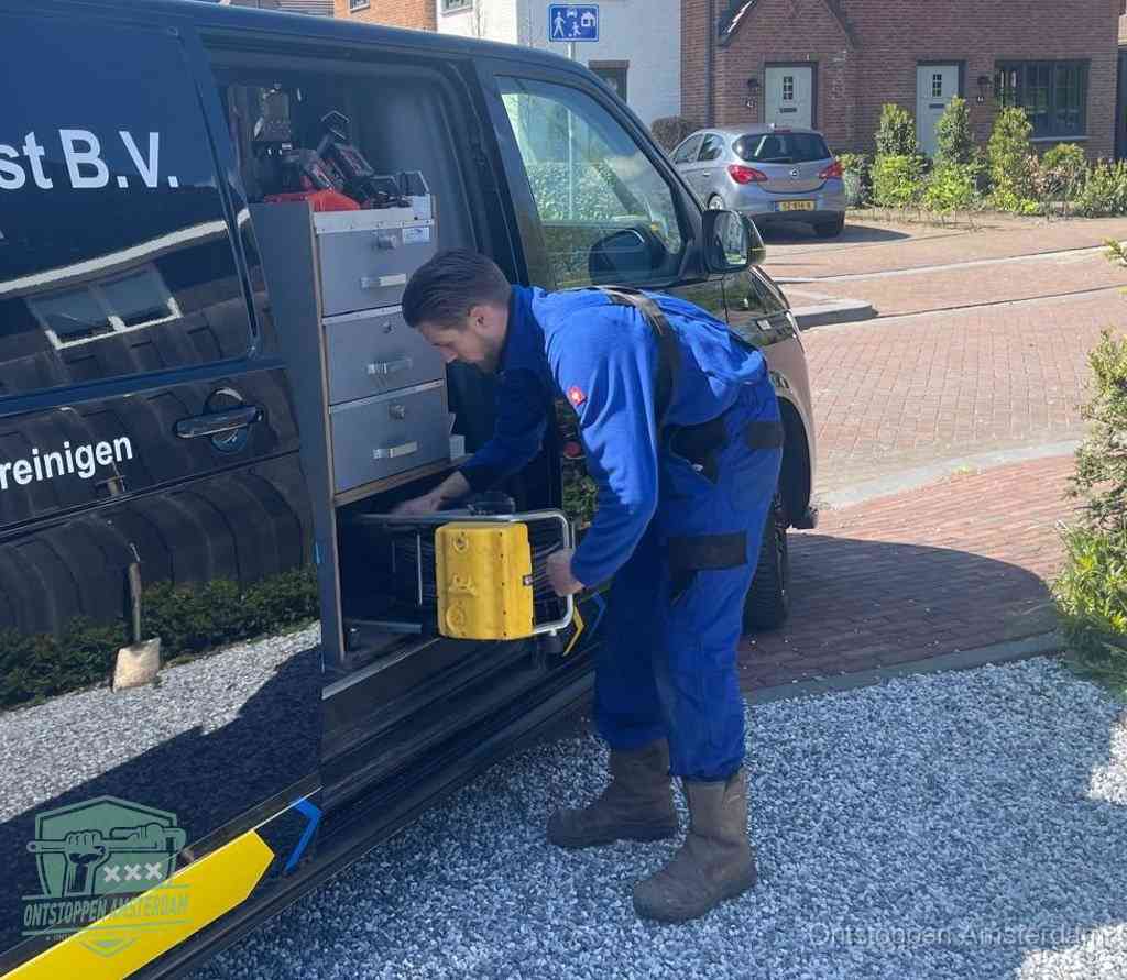 Een monteur pakt buiten op de oprit gereedschap uit de bedrijfsbus, het moment om een professional in te schakelen voor een verstopte afvoer in Amsterdam