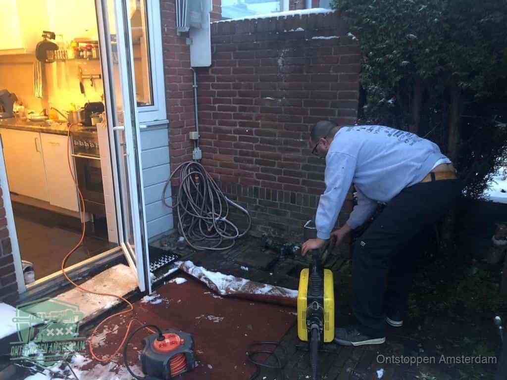 Een monteur werkt buiten bij een open riool-/grondput met een elektrische ontstoppingsmachine om een verborgen afvoerprobleem op te sporen in Amsterdam