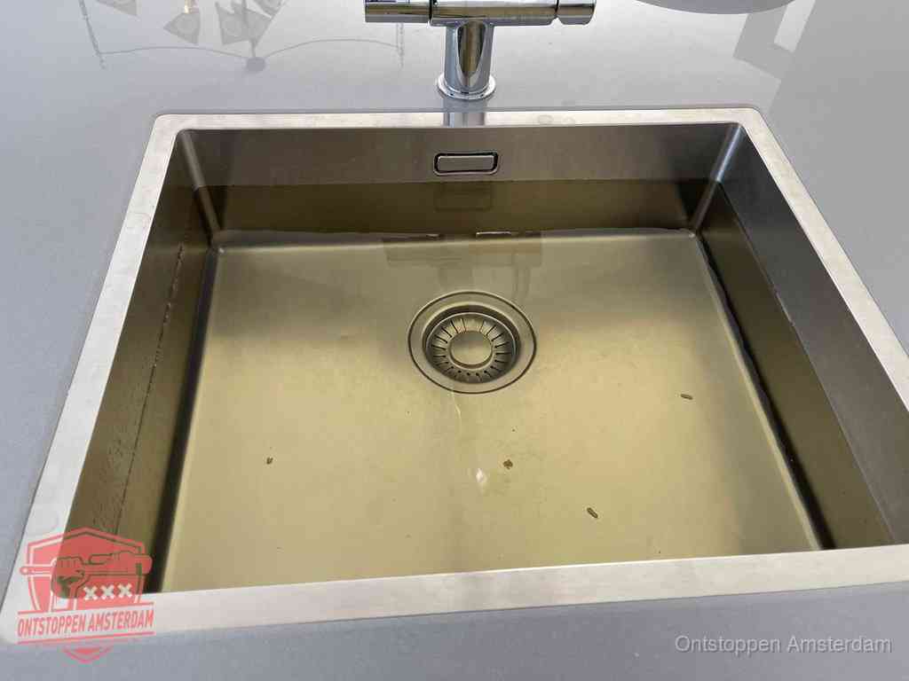 Stilstaand water in een rvs spoelbak dat niet wegloopt, een duidelijk signaal van een gootsteenverstopping in Amsterdam