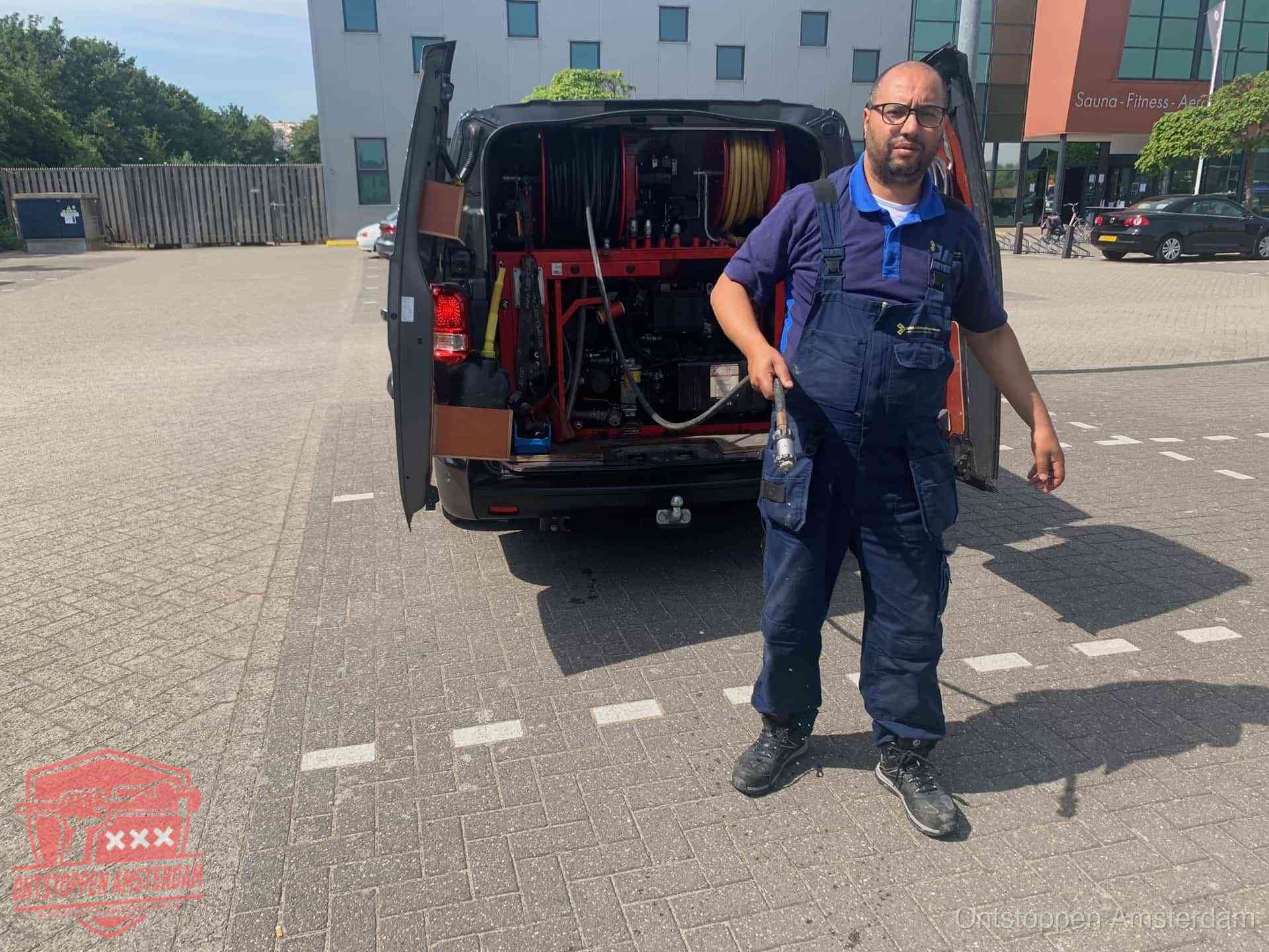 Een monteur bij zijn bestelbus met een hogedruk- en rioolreinigingsunit, klaar om de oorzaak van terugkerende wc-verstoppingen aan te pakken in Amsterdam