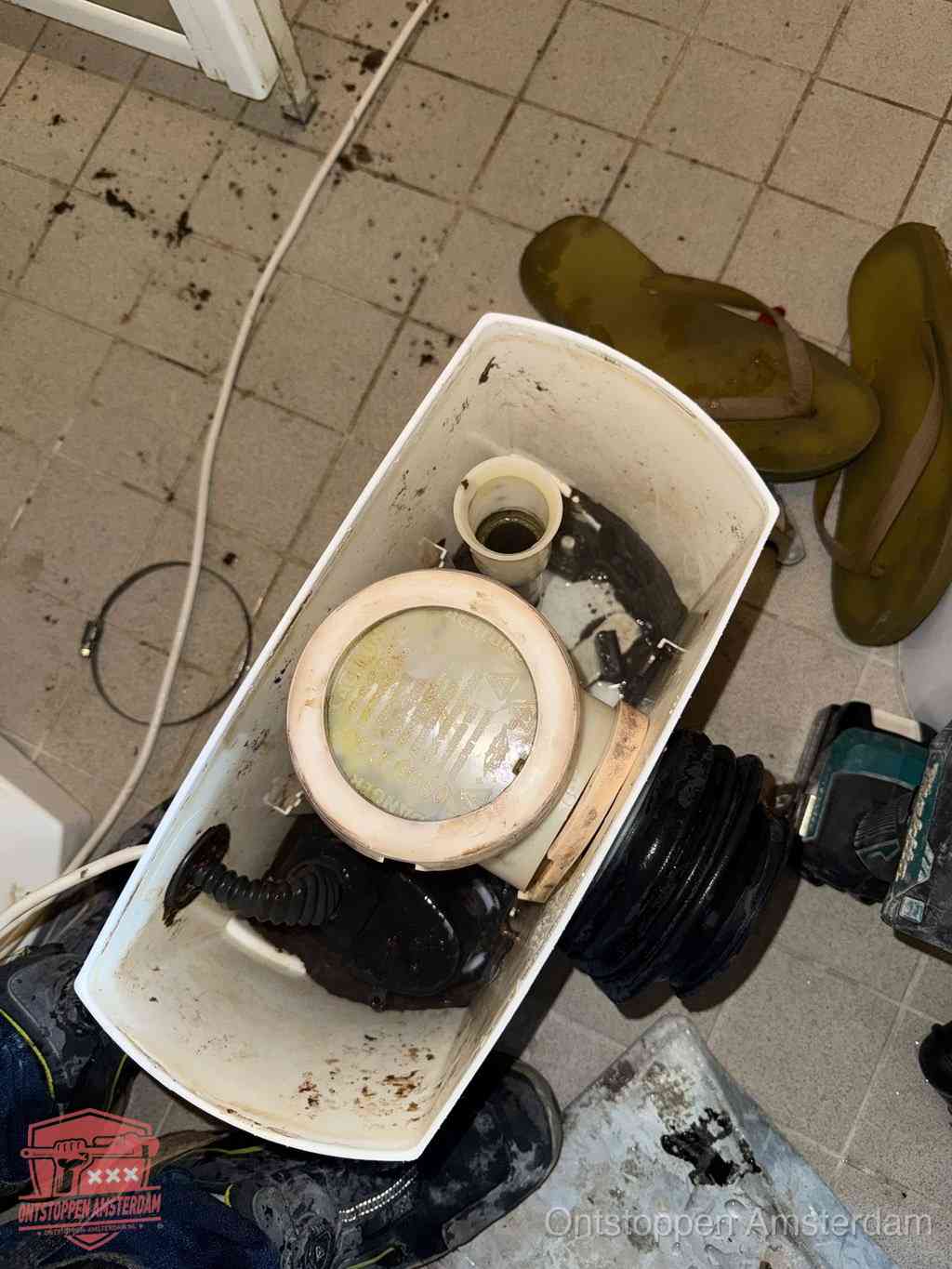 Een gedemonteerde toiletpot op de vloer met ontstoppingsveer en gereedschap ernaast, het verwijderen van een vastzittend voorwerp uit de wc in Amsterdam