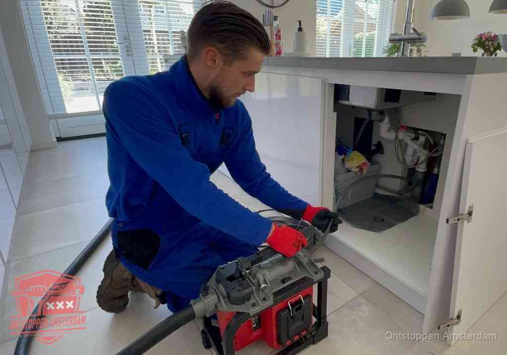 Een monteur voert een professionele elektrische ontstoppingsmachine in de afvoer onder de spoelbak tijdens het gootsteen ontstoppen in Amsterdam